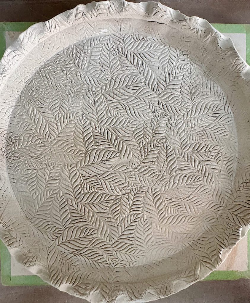 A round piece of dough with crimped edges and a detailed leaf pattern pressed across its surface.