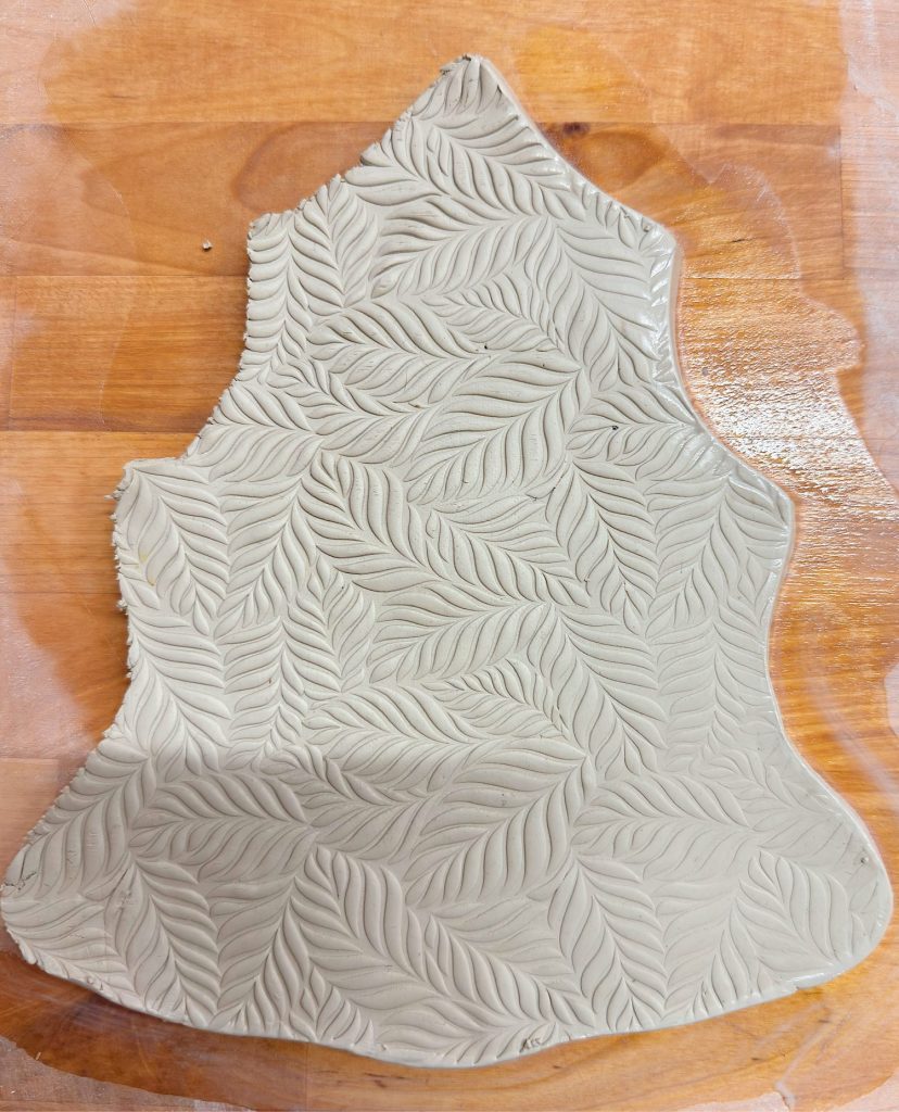 A slab of light gray clay with an embossed leaf pattern lies on a wooden surface.