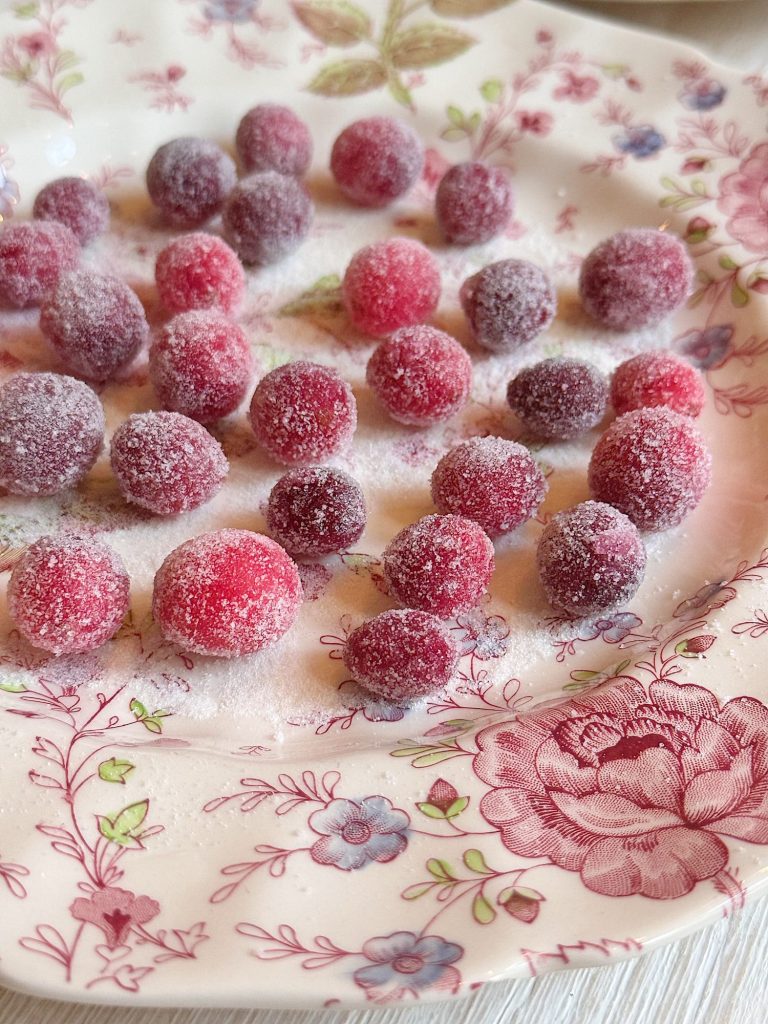 A decorative floral plate with sugared cranberries evenly spread across its surface.