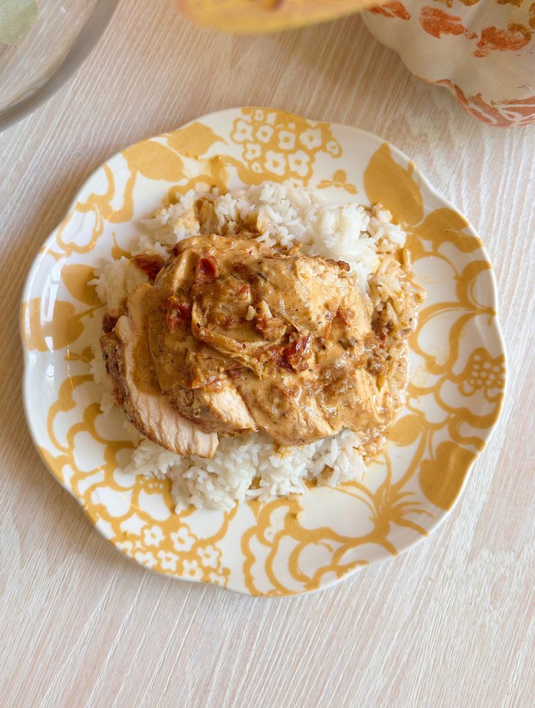 A serving of cooked rice topped with sliced chicken breast and a creamy sauce on a yellow patterned plate.