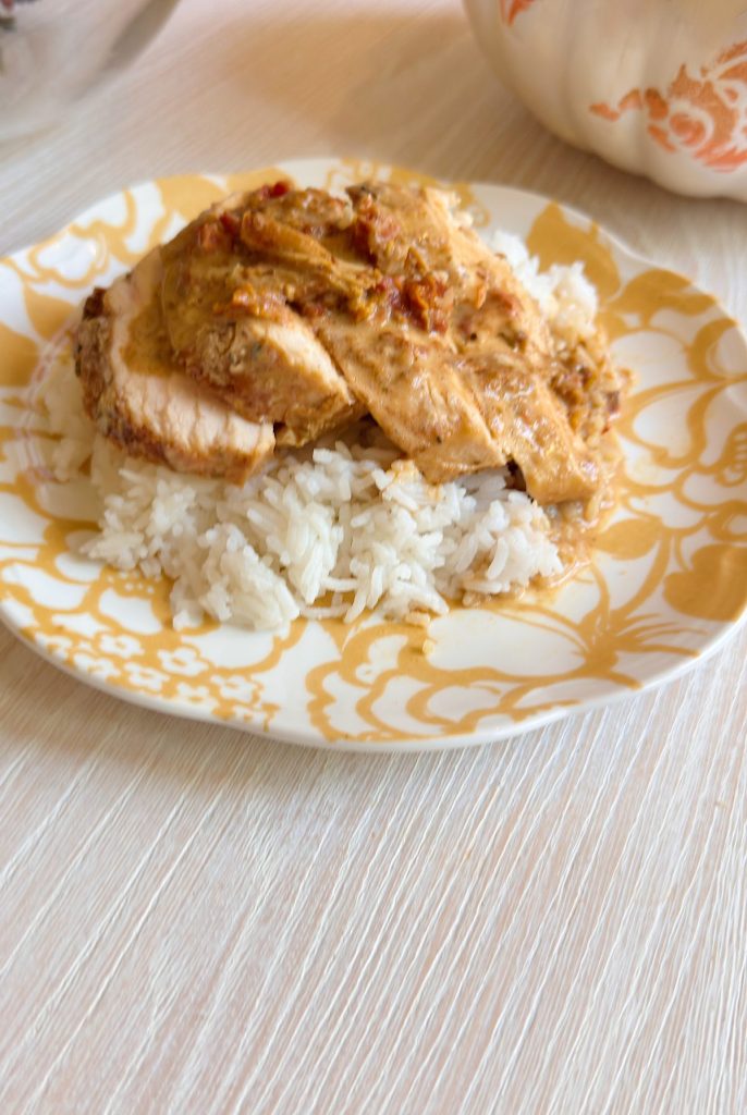 Sliced chicken breast with creamy sauce served over a bed of white rice on a patterned plate.