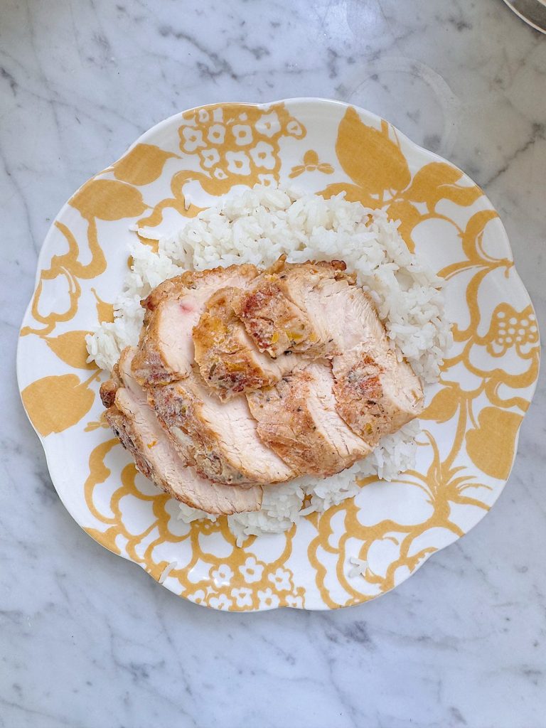 A plate with white rice topped with several slices of roasted chicken, placed on a yellow and white patterned dish.