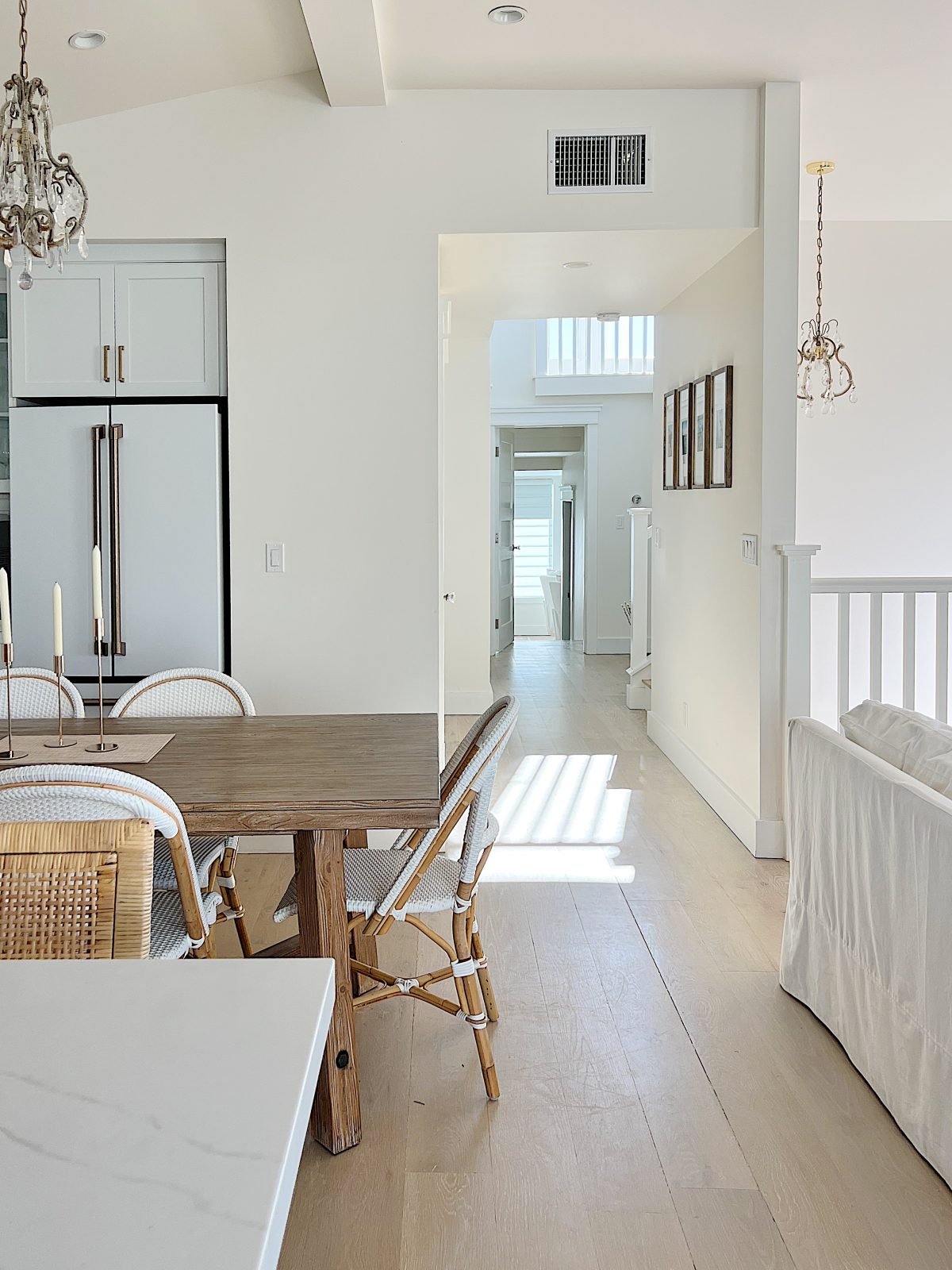 Bright, modern dining and living area with wooden table, white chairs, and natural light streaming through hallway into a minimalist kitchen&mdash;perfect for relaxing after a day of shopping on Amazon Prime.