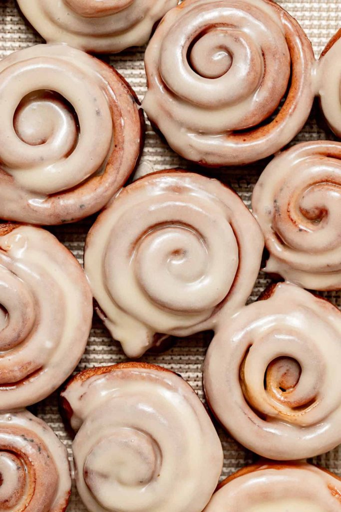 Close-up of several cinnamon rolls arranged together, each topped with a smooth layer of white icing.