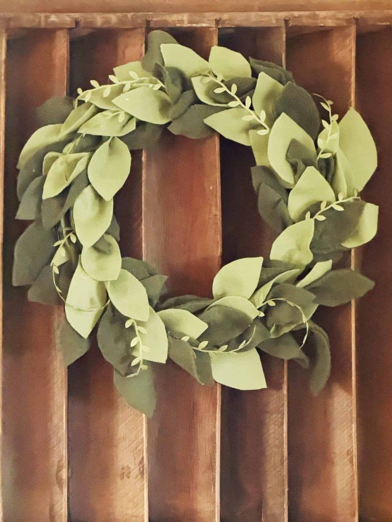 A wreath made of green fabric leaves hangs on a wooden slatted wall.
