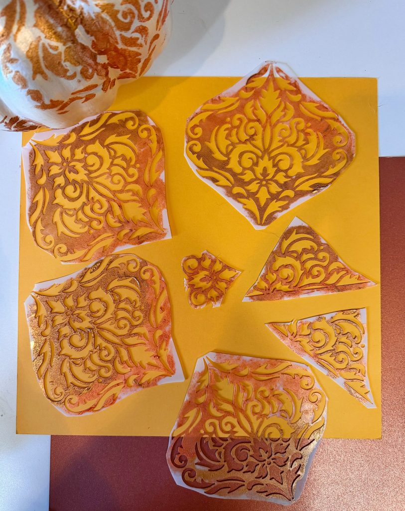 Seven pieces of orange and gold ornate patterned paper are arranged on a yellow square sheet, with part of a similarly patterned sphere visible in the upper left corner.