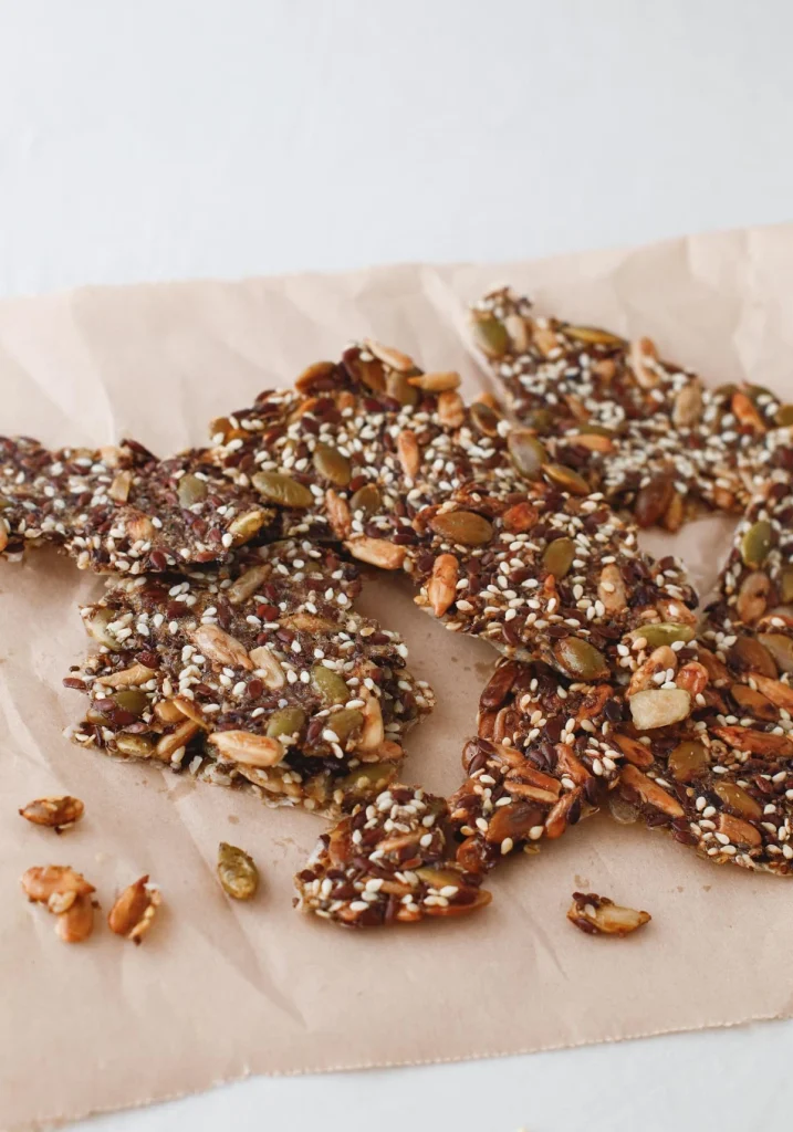 Crispy seed crackers with sesame, pumpkin, and sunflower seeds are scattered on a piece of parchment paper.