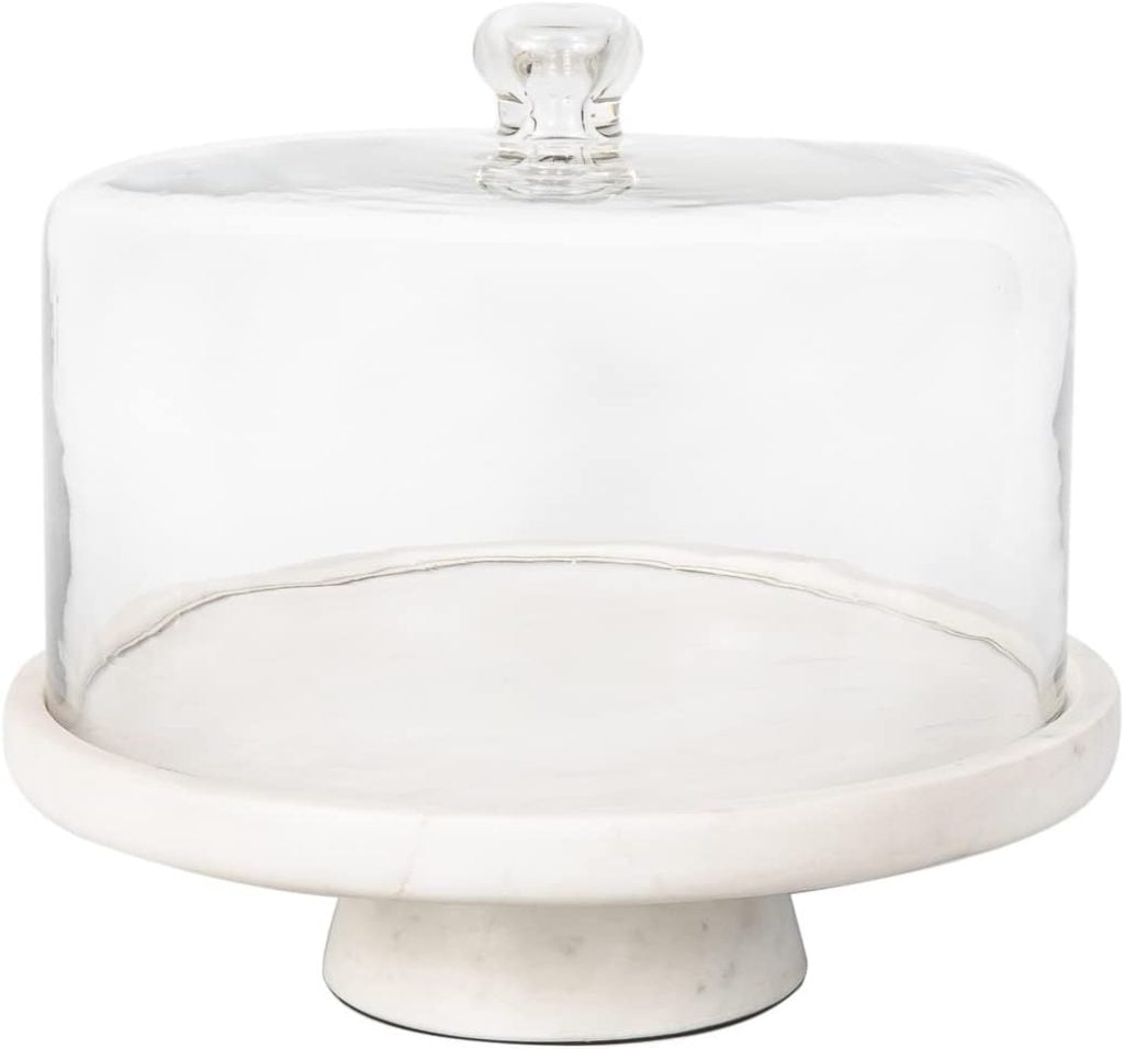 A white marble cake stand with a round base and clear glass dome lid, perfect for showcasing desserts in blog posts, photographed against a plain white background.