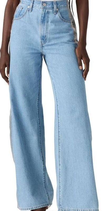A person wearing high-waisted, light blue wide-leg jeans, a white top, and open-toe heeled sandals stands against a plain background—perfect style inspiration for Black Friday shopping.
