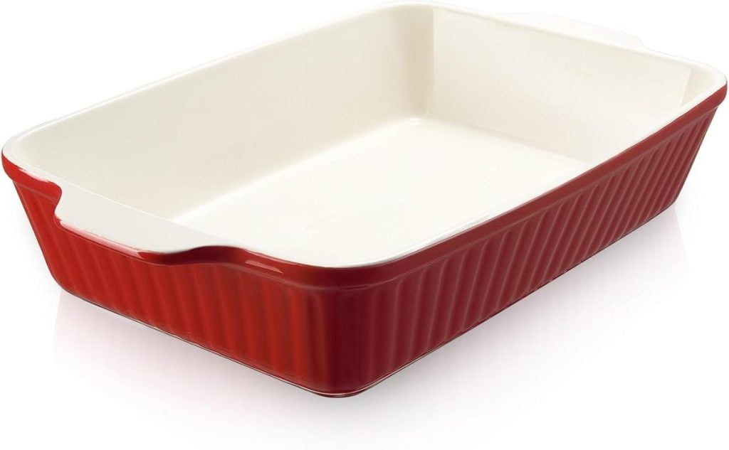 Red rectangular ceramic baking dish with white interior, shown empty and angled to display the ridged exterior and built-in handles.