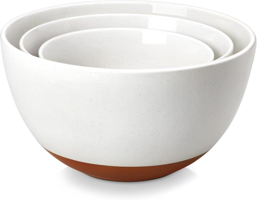 Three white ceramic mixing bowls of different sizes are nested together, with a brown base visible on the largest bowl.