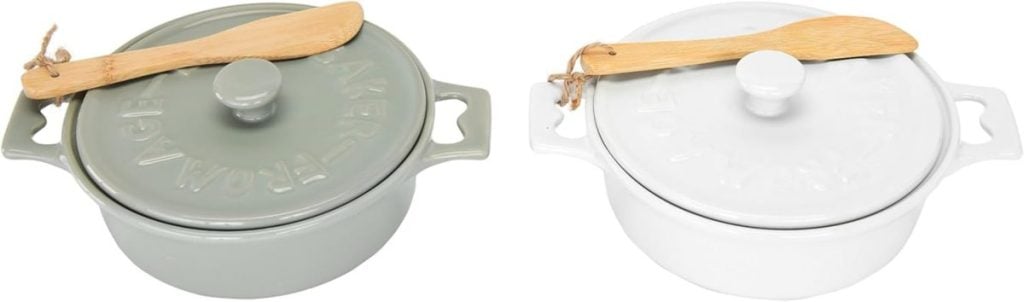 Two ceramic baking dishes with lids, one grey and one white, each with a wooden spreading knife resting on top.