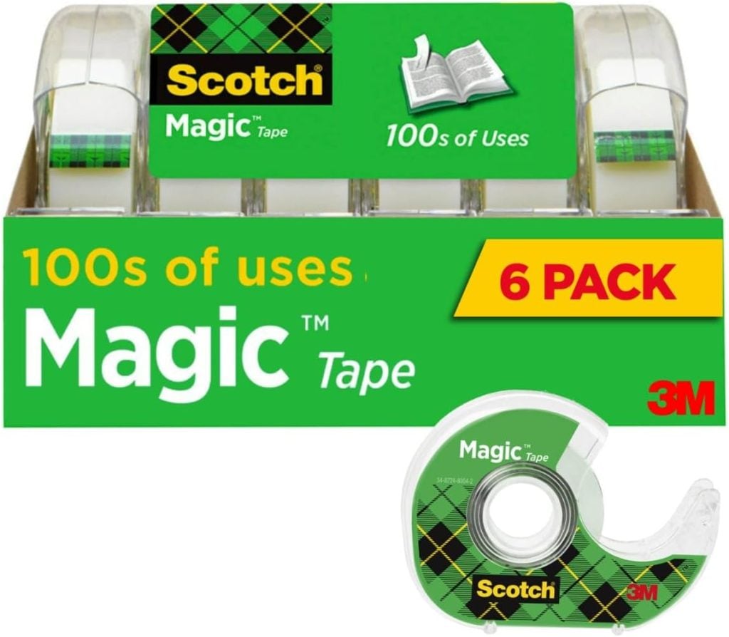 A box of six rolls of Scotch Magic Tape by 3M, labeled "100s of Uses" and "6 Pack," with one tape dispenser shown in the foreground—perfect for crafts like window art.