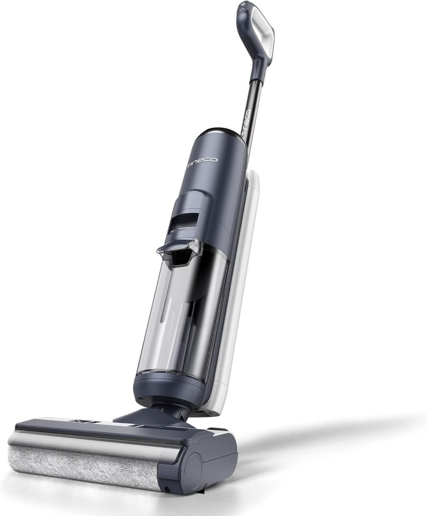 A cordless upright vacuum cleaner with a transparent dustbin, a handle, and a wide roller cleaning head, shown standing upright on a white background.