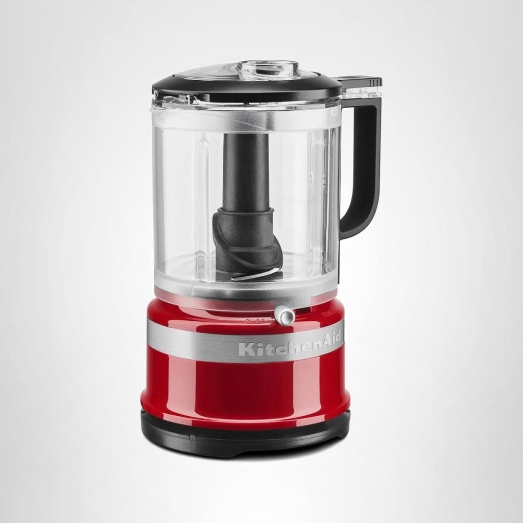 A red and silver KitchenAid food processor with a clear plastic container and black handle, set against a plain white background.