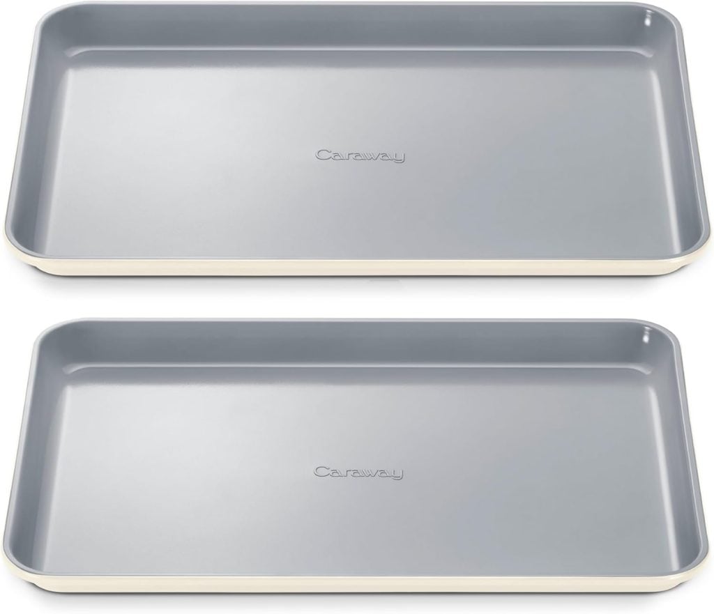 Two rectangular, gray nonstick baking sheets with slightly raised edges, stacked side by side. The word "Caraway" is embossed in the center of each tray.