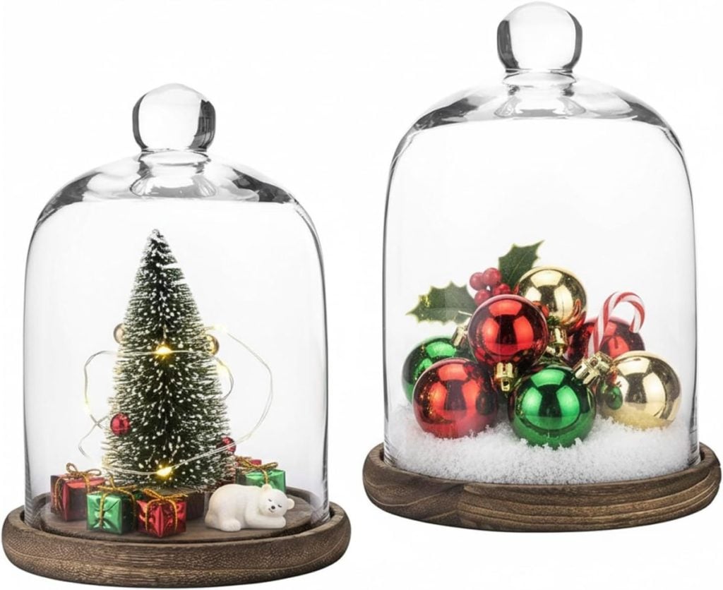 Two glass cloches on wooden bases; one contains a miniature Christmas tree with presents and a bear figurine, the other holds festive ornaments and faux snow.