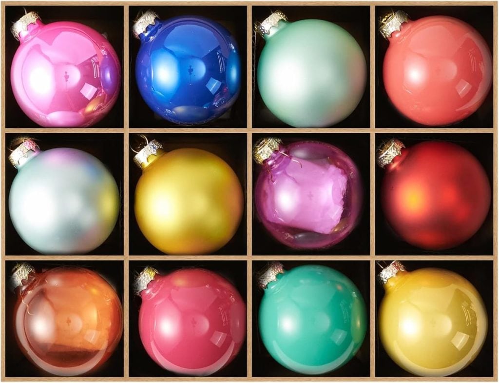 Twelve shiny Christmas ornaments in various colors are arranged in a 3x4 grid within a wooden box.