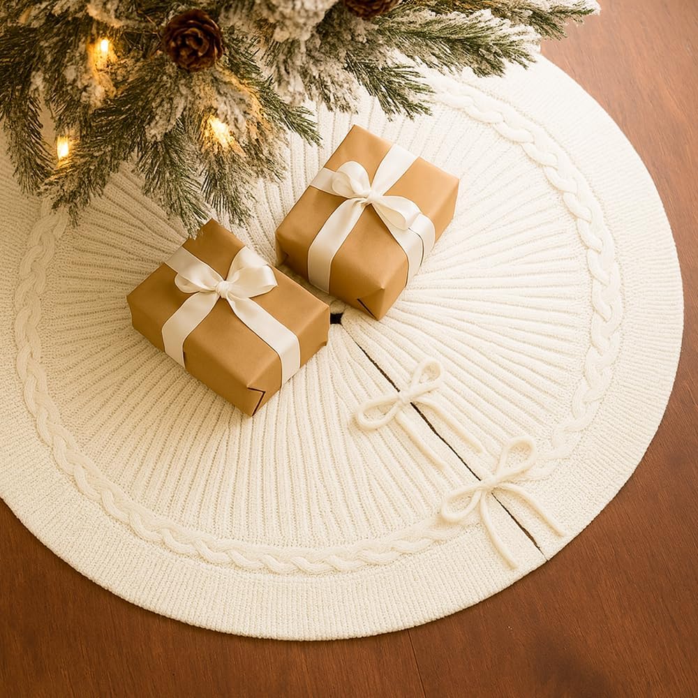 Two gift boxes with white ribbons sit on a cream-colored knitted tree skirt under a decorated Christmas tree with lights.
