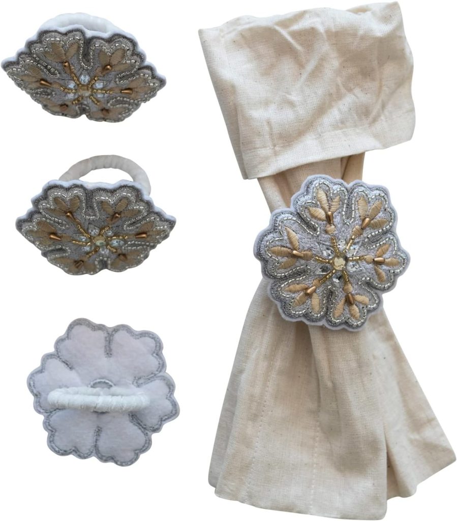 Four views of an ornate, floral-patterned napkin ring in silver and gold, shown alone and holding a folded beige cloth napkin.