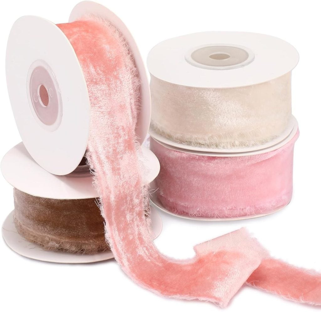Four spools of velvet ribbon in shades of pink, cream, and brown are arranged together, with one pink ribbon partially unrolled in front.