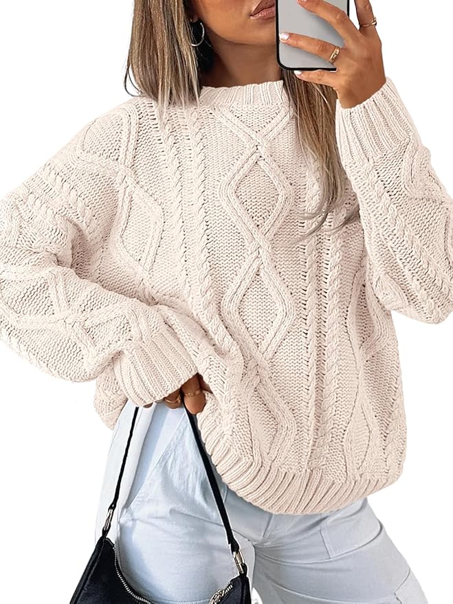 A person wearing a cream-colored, cable-knit sweater holds a phone in one hand and a black bag in the other, long hair partially covering their face, reminiscent of cozy days spent decorating with mercury glass ornaments.