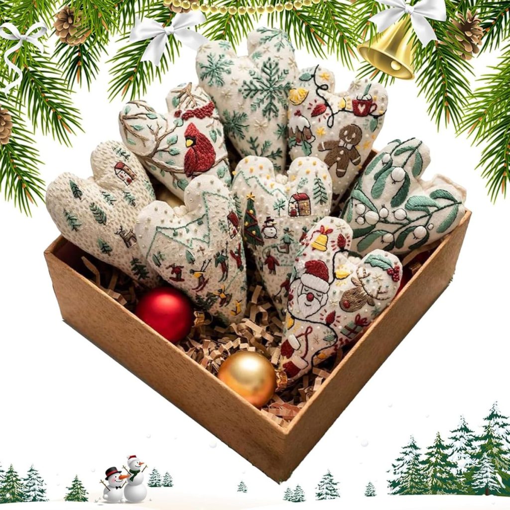 A box of fabric heart ornaments with Christmas patterns, placed on straw with red and gold baubles, surrounded by festive pine and bell decorations.