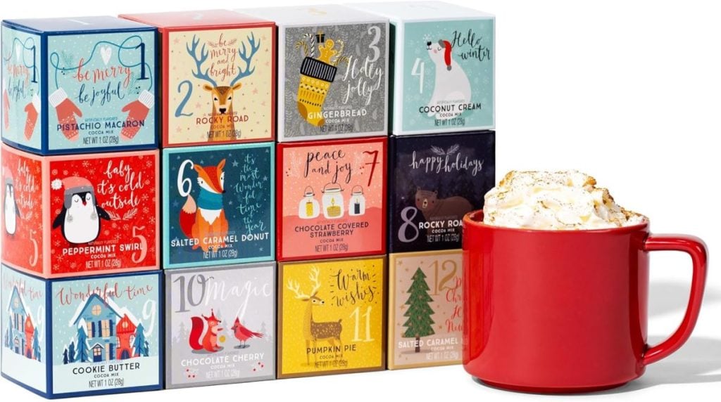 A red mug filled with whipped cream sits next to a 12-day holiday-themed chocolate advent calendar with illustrated designs on each box.