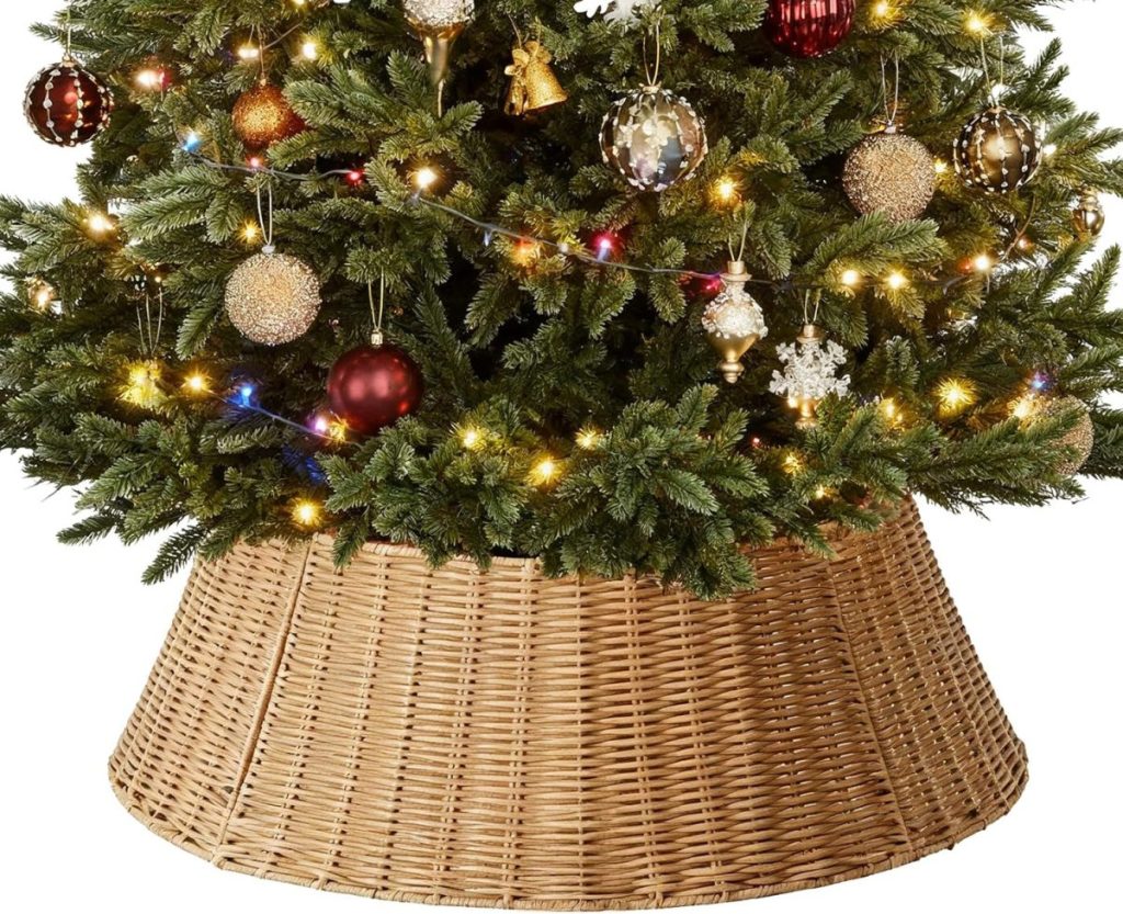 The base of a decorated Christmas tree with lights and ornaments is shown inside a woven wicker tree collar.