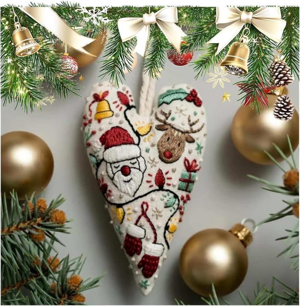 A fabric heart ornament with Santa and a reindeer design hangs surrounded by gold baubles, pine branches, and Christmas decorations.
