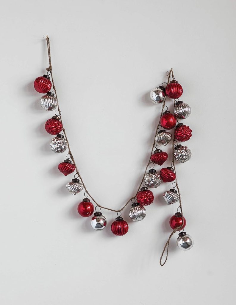 A garland made of red and silver Mercury Glass Ornaments is hung on a white wall.