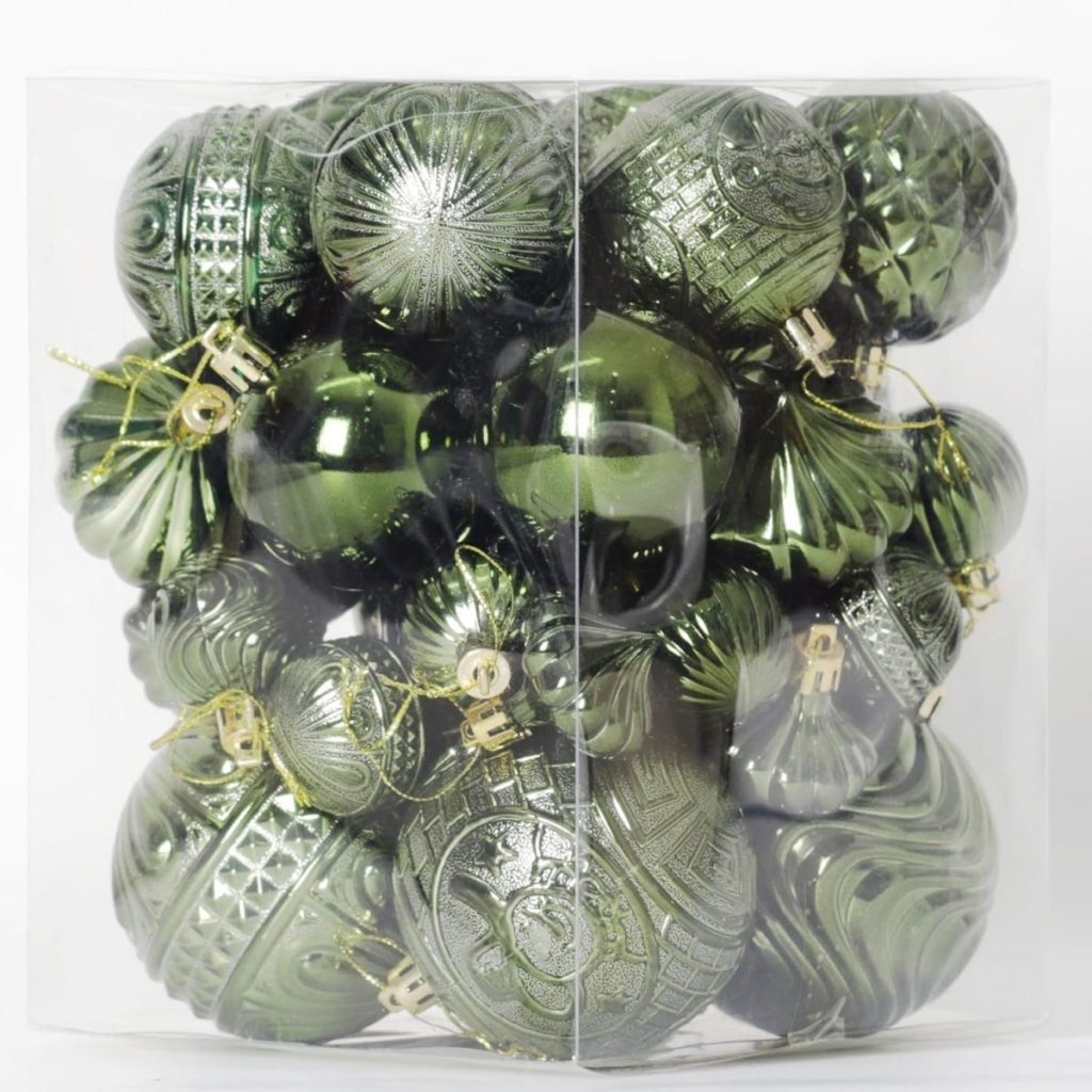A clear plastic box filled with various shiny and textured green Christmas tree ornaments.