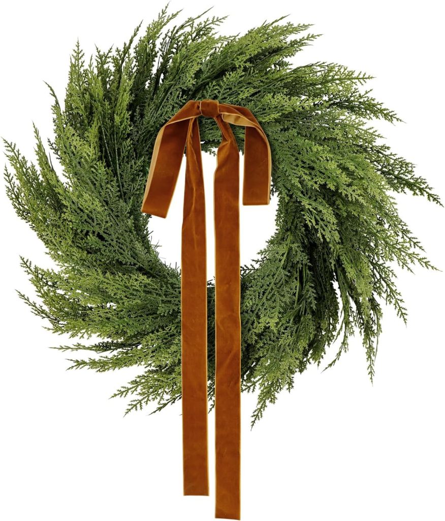 A circular green wreath made of pine branches, adorned with a long, brown velvet ribbon tied in a bow at the top.