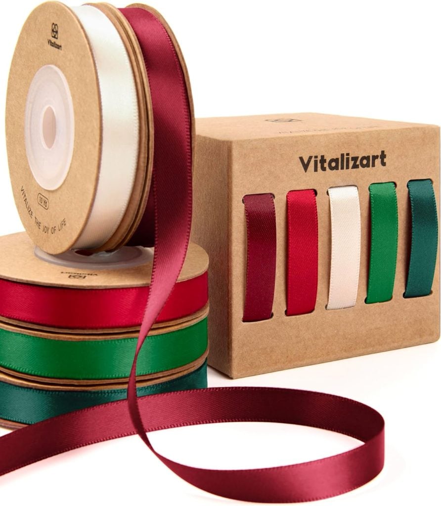 Four spools of colored satin ribbon (red, white, green, burgundy) are displayed next to a box labeled "Vitalizart" that shows ribbon samples on the side.