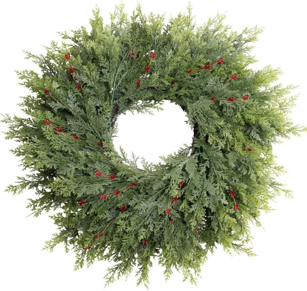 A circular green wreath made of evergreen branches, decorated with small red berries, photographed against a white background—perfect as festive window art.