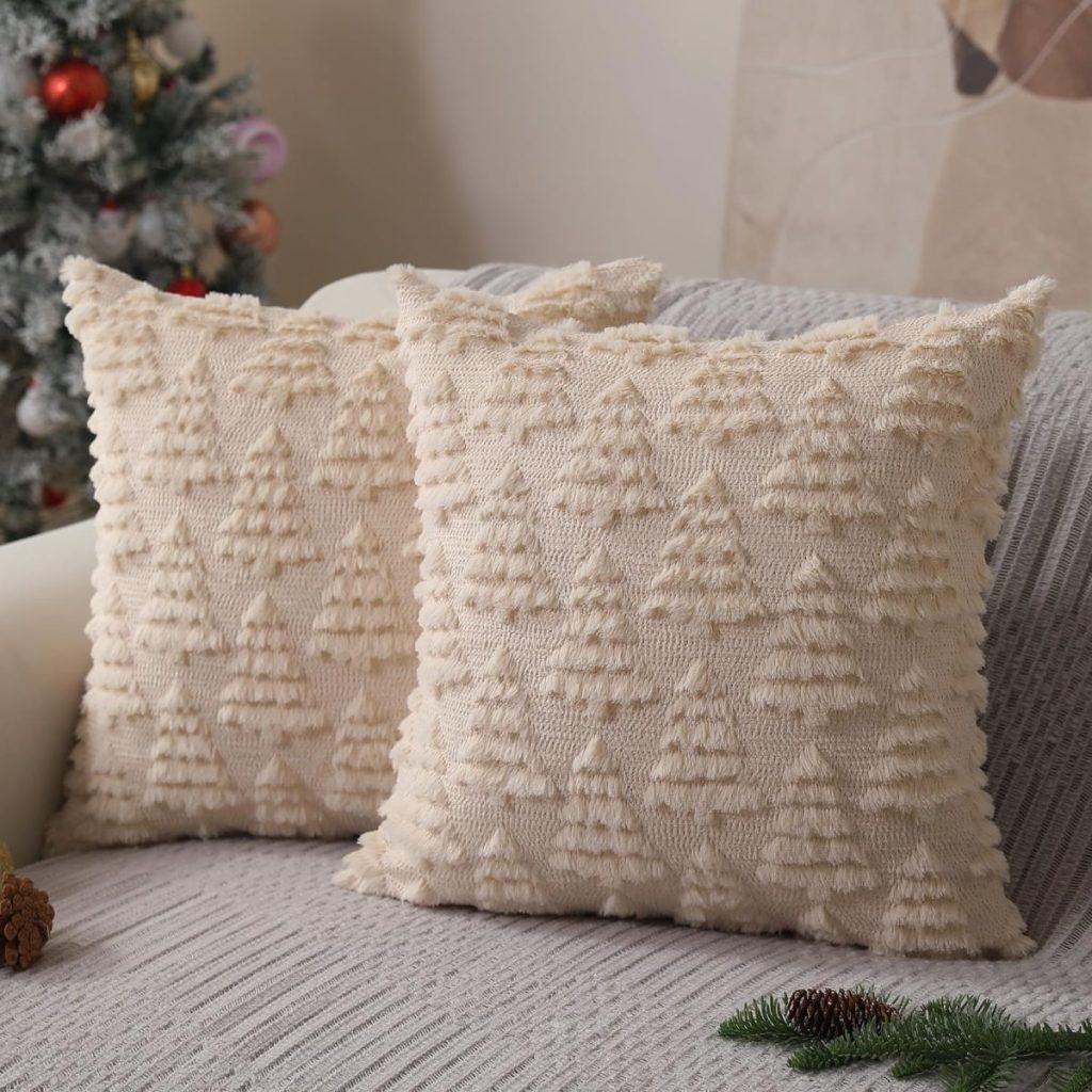 Two beige throw pillows with textured Christmas tree patterns rest on a light gray sofa, with a decorated Christmas tree visible in the background.