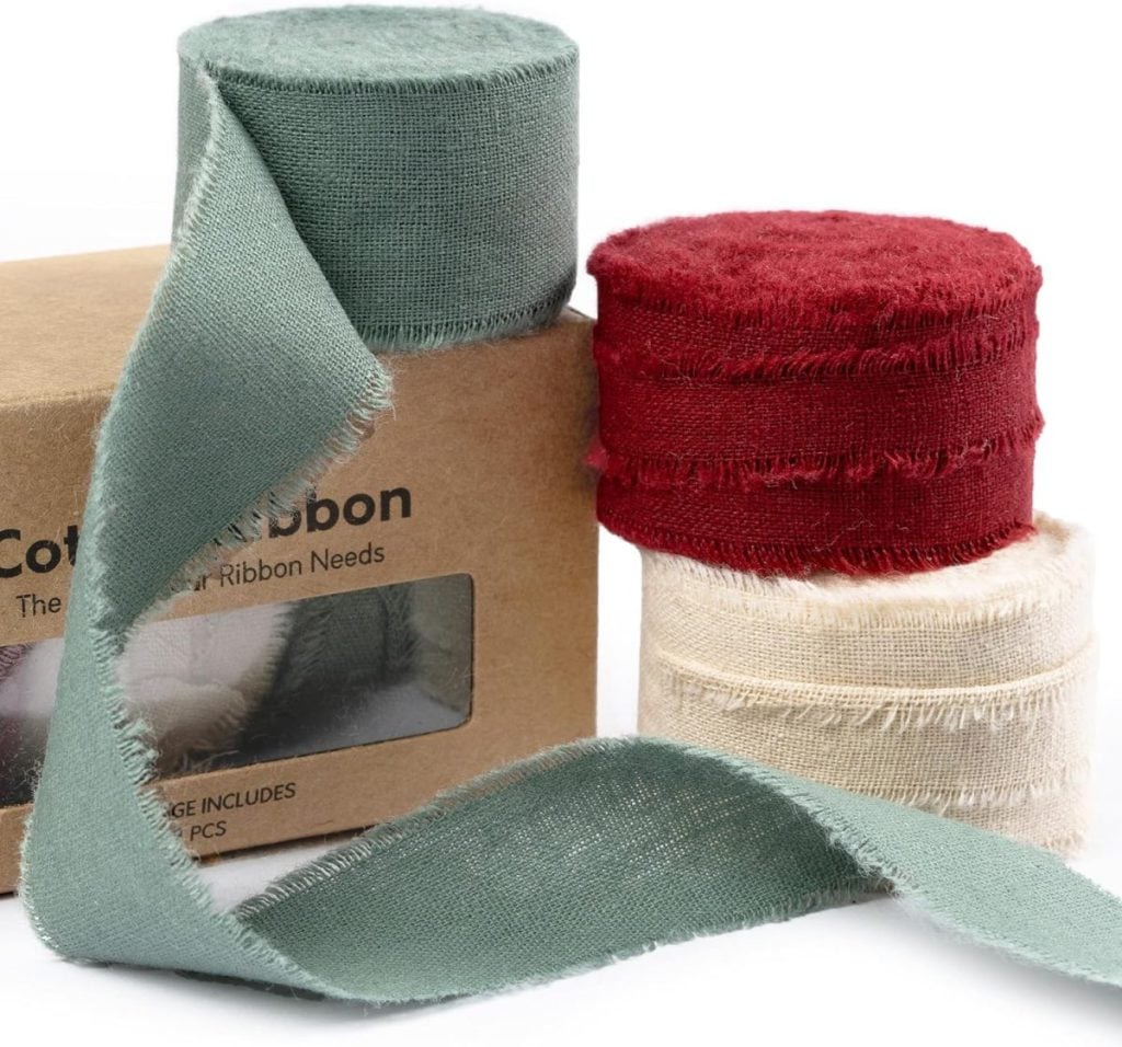Three rolls of frayed edge fabric ribbon in green, red, and cream are displayed next to a brown cardboard box with a clear window.