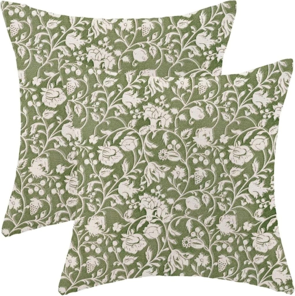 Two green square throw pillows with a white floral pattern overlapping each other on a white background.