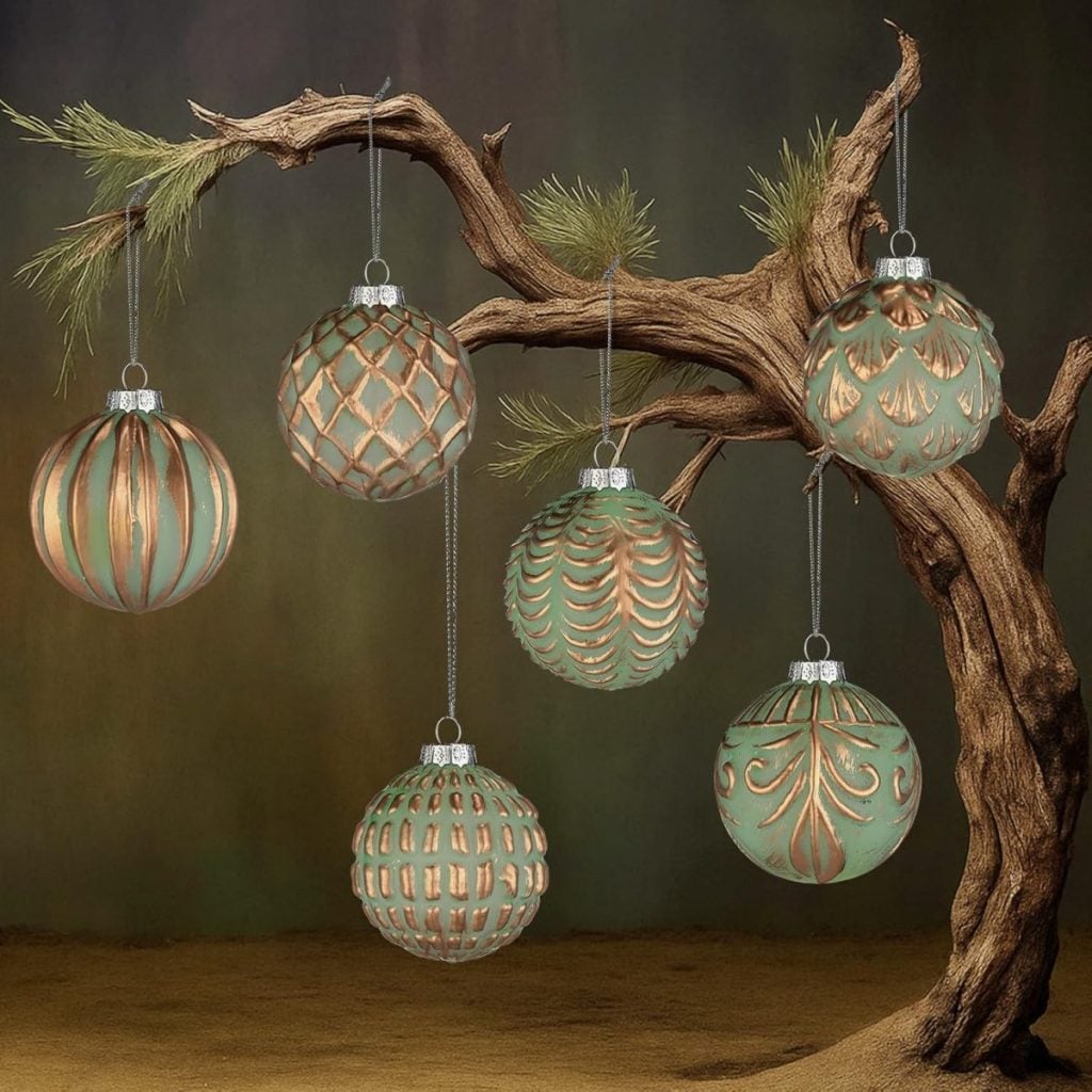 Six green and gold Christmas ornaments with various patterns hang from the branches of a bare, stylized tree against a muted background.