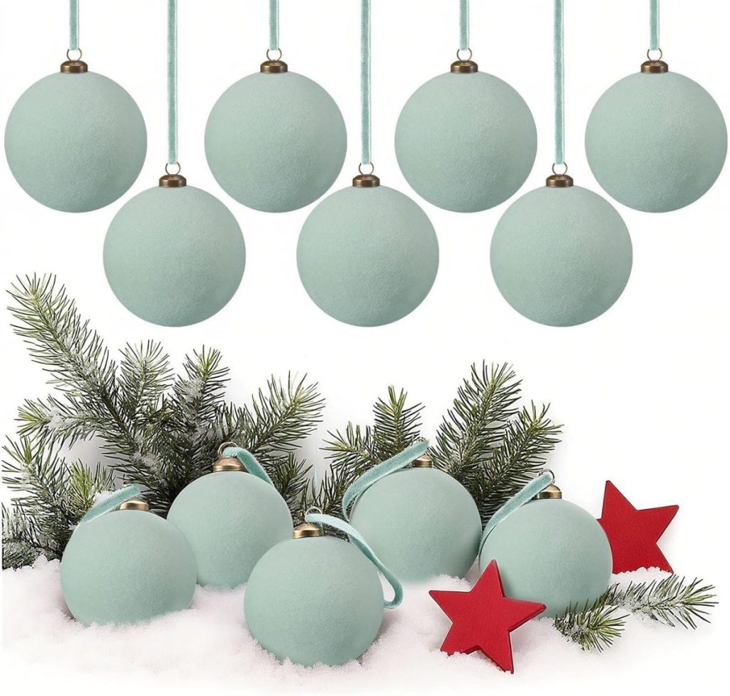 Light blue Christmas ornaments and red star decorations are arranged on pine branches and snow, with additional ornaments hanging above.