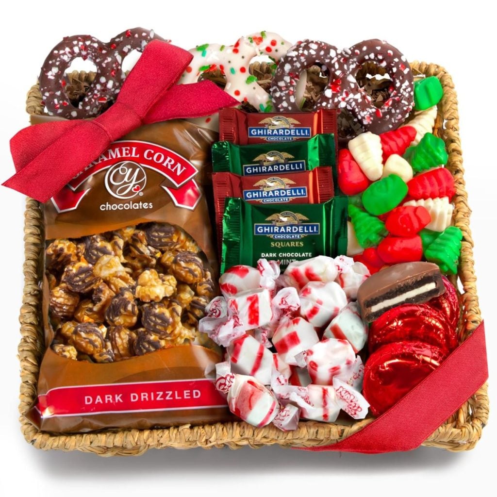 A gift basket with caramel popcorn, Ghirardelli chocolates, peppermint candies, chocolate coins, holiday pretzels, and gummy candies, all tied with a red ribbon.