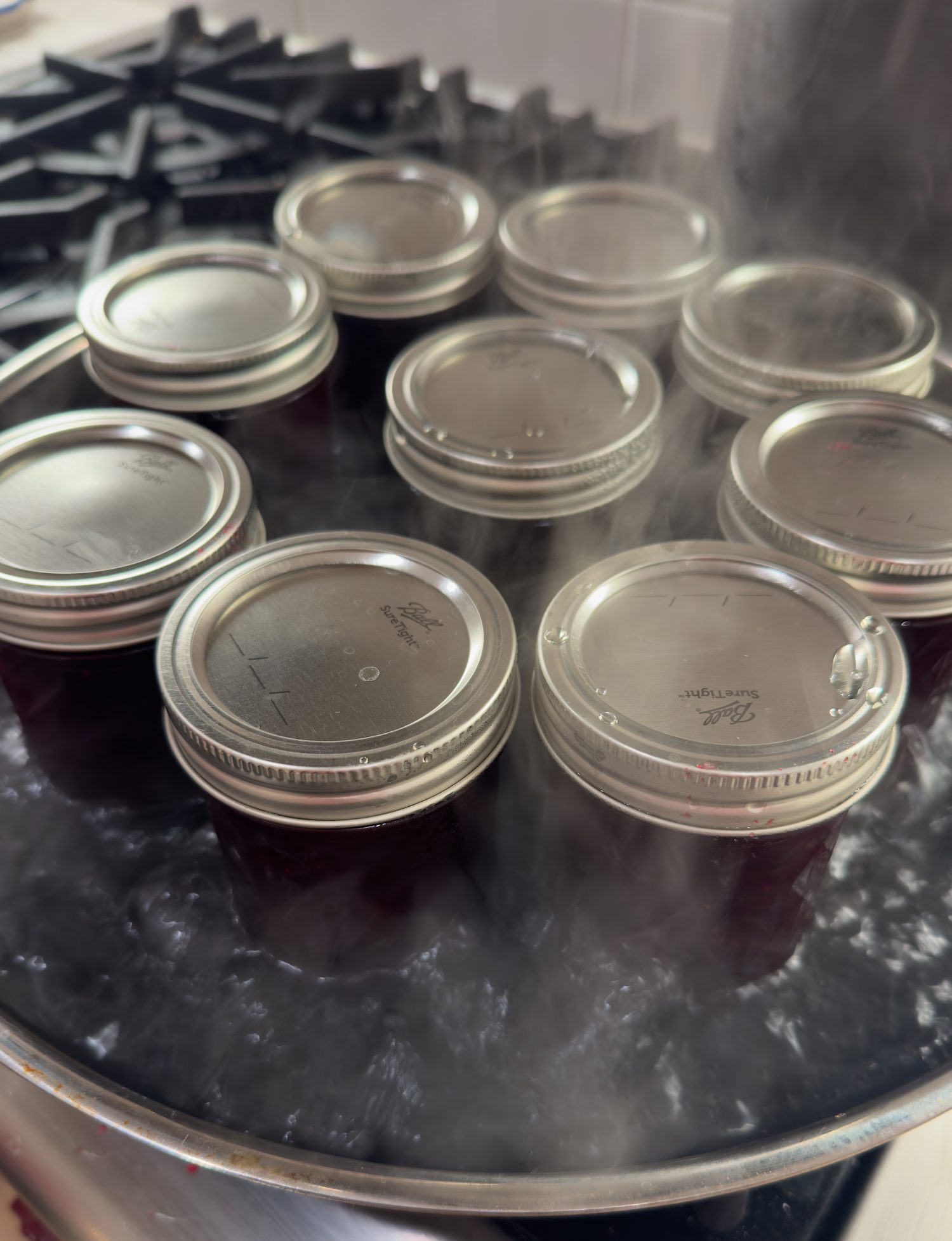 Several glass jars with metal lids are being sterilized in a boiling water bath, with steam rising around them.