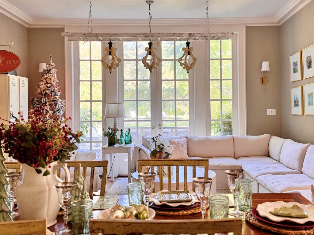 A sunlit living and dining room with a set dining table, a white sectional sofa, large windows, and a decorated Christmas tree.