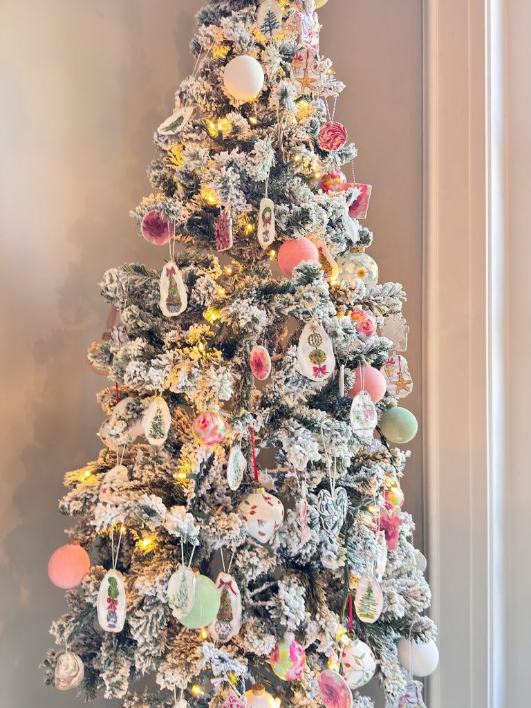 A flocked Christmas tree, adorned with assorted colorful ornaments and warm white string lights, brings festive Christmas decor to the space as it stands by a window.
