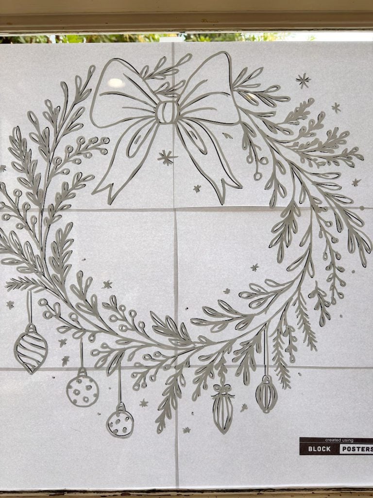 Black and white line drawing of a holiday wreath with a large bow, hanging ornaments, and scattered stars, displayed on a tiled background.
