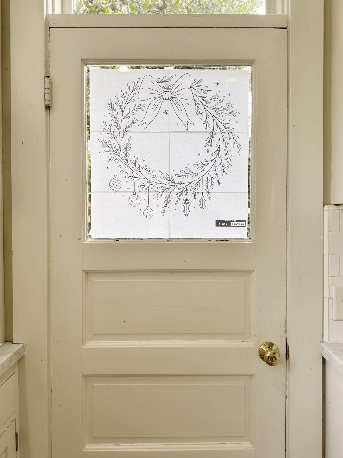 A white door with a frosted glass window decorated with a line drawing of a holiday wreath, bow, and hanging ornaments.