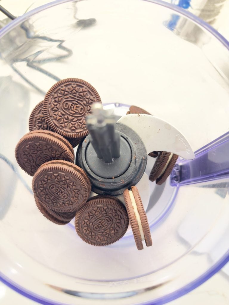 Oreo cookies placed inside a food processor, ready to be crushed with the metal blade attachment visible in the center.