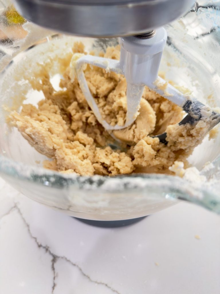 Electric stand mixer with dough being mixed in a glass bowl, placed on a white marble countertop.