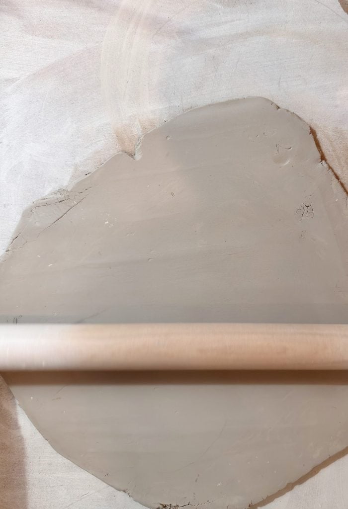 A rolling pin lies on a flat, smooth sheet of clay on a light-colored surface.