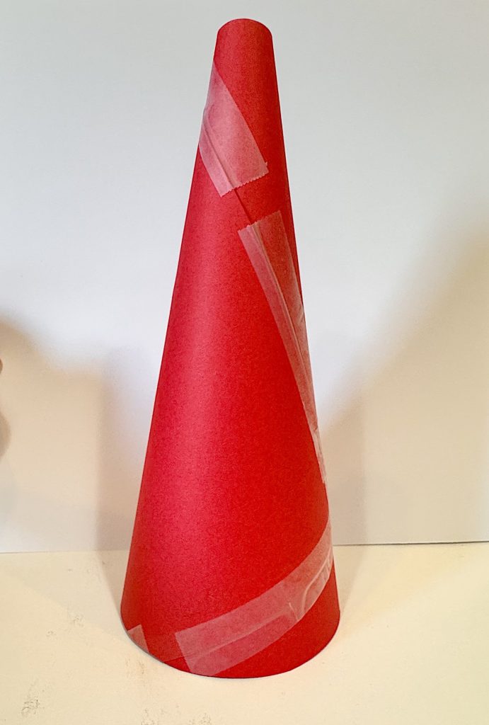 A red paper cone stands upright on a white surface, secured with pieces of clear tape.